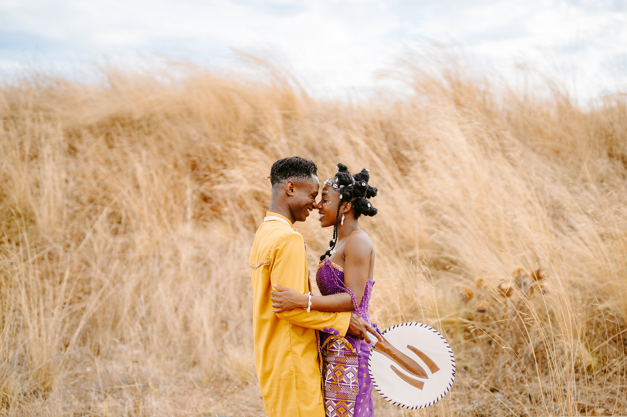 Pearl and Allen rest forehead to forehead in a field of golden grass, fans in hand.